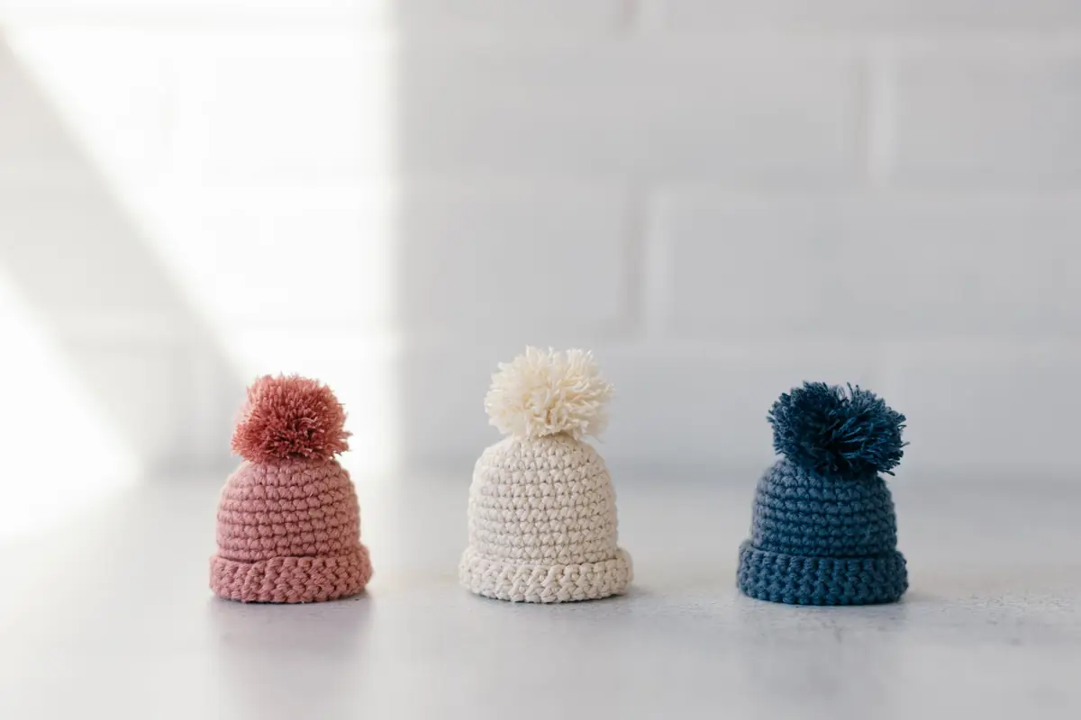 Hand-crocheted hats laid out in cream, blue, and pink.