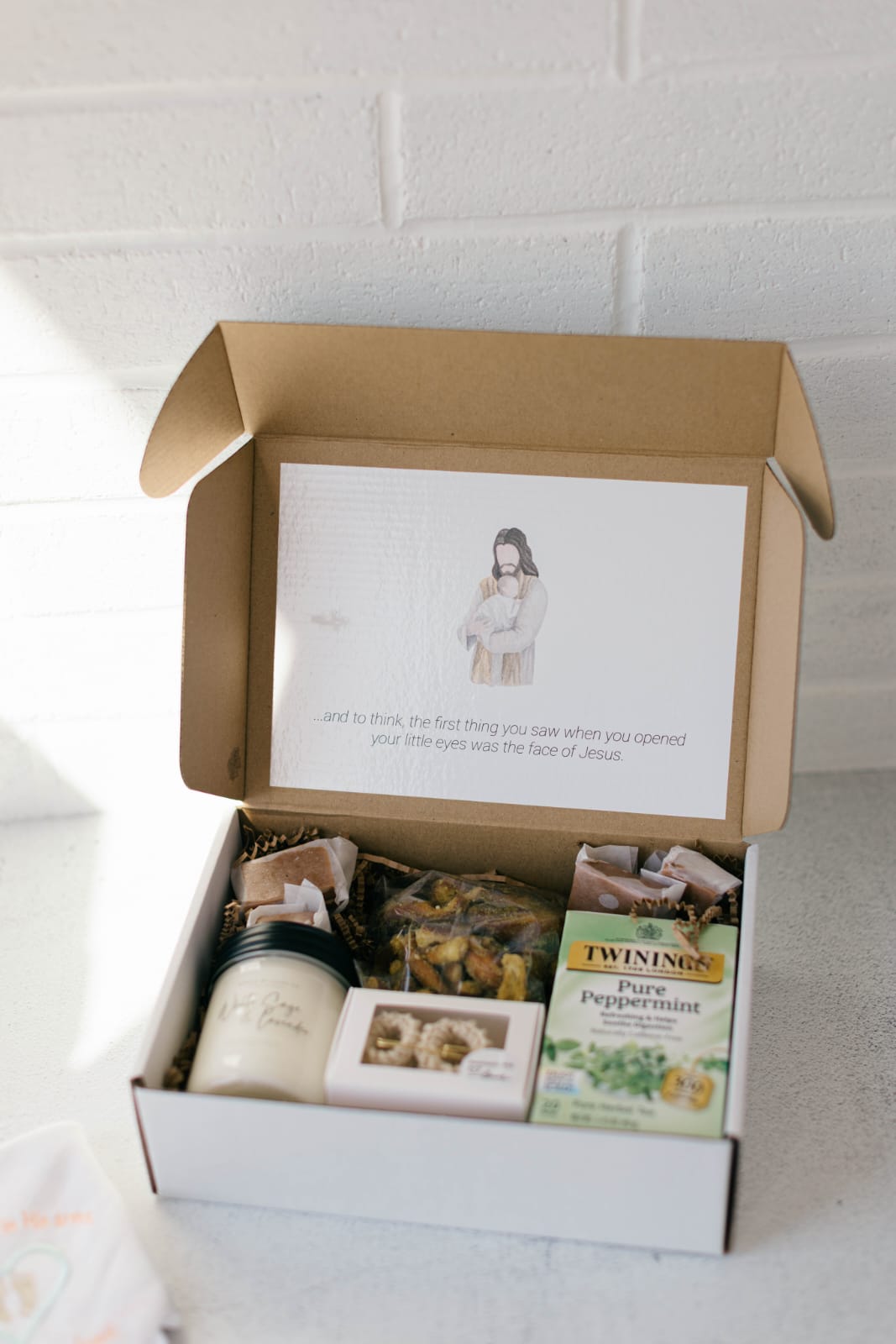 Comfort & Keepsake — Crocheted baby booties (cream, blue, or pink), a jar candle, caramels & pretzels, a box of tea, and a diaper.