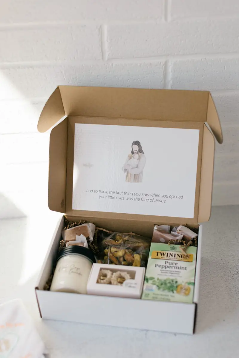 Comfort & Keepsake — Crocheted baby booties (cream, blue, or pink), a jar candle, caramels & pretzels, a box of tea, and a diaper.